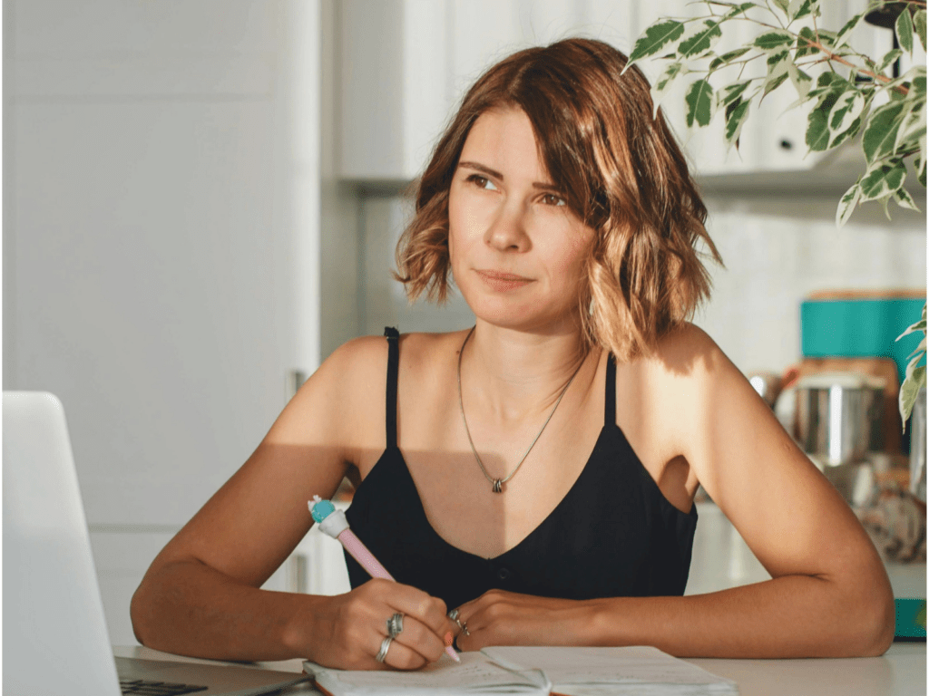 eine weiße Frau hält einen Stift in der Hand und blickt nachdenklich in die Ferne