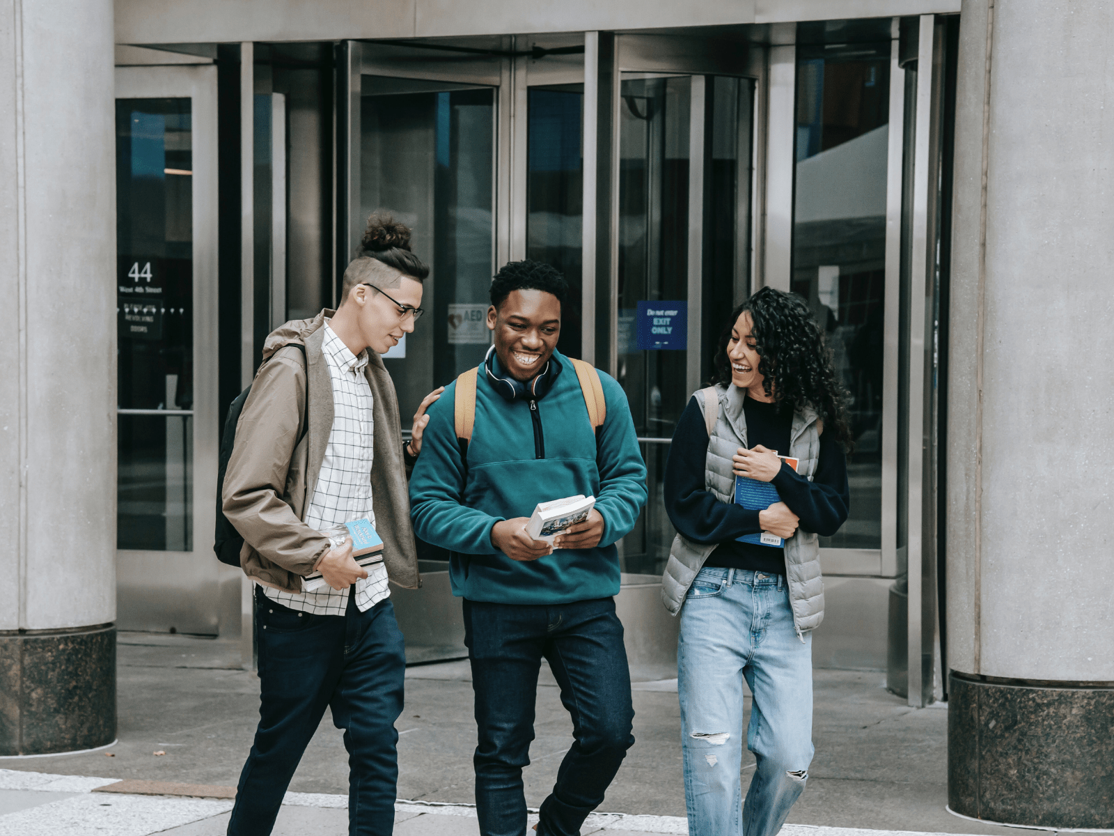 drei junge Personen verlassen lachend ein Gebäude für Bildungsangebote für Menschen mit Flucht und Migrationserfahrung
