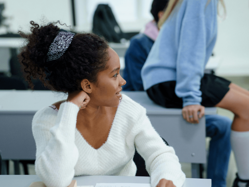 eine Schwarze Schüler*innen sitzt im Klassenraum und hält einen Stift