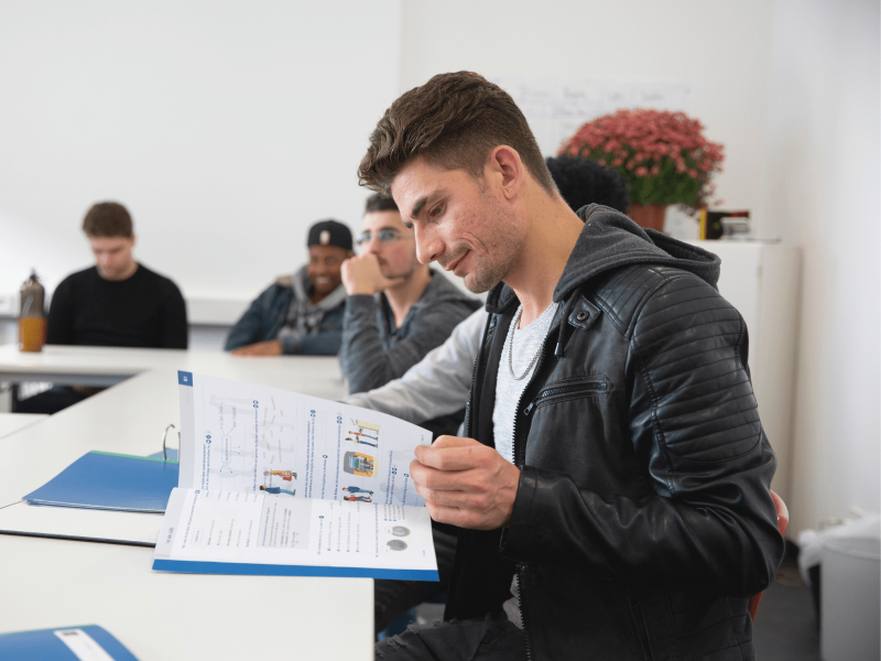 Schüler sitzt im Klassenraum und blättert durch DaZ-Lernmaterial