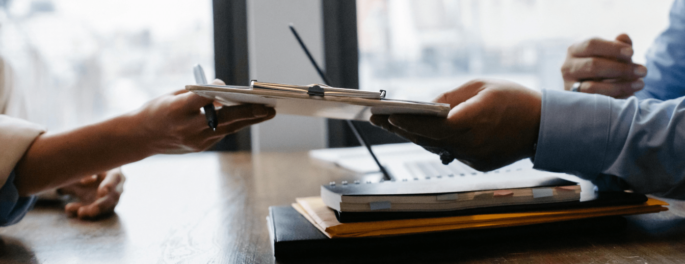 eine Hand überreicht ein Formular bei einem Bewerbungsgespräch