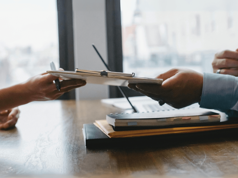 eine Hand überreicht ein Formular bei einem Bewerbungsgespräch
