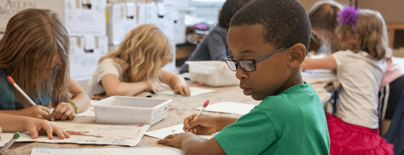 An einem Tisch sitzen diverse Grundschüler und Grundschülerinnen und malen etwas