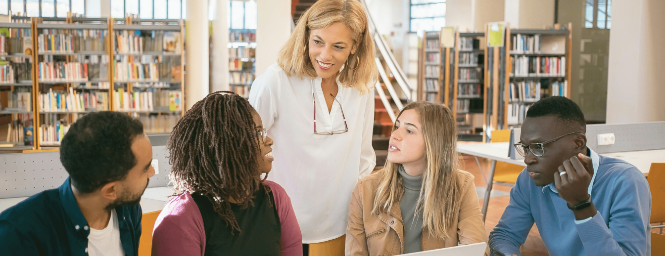 eine Lehrkraft beugt sich lächelnd über eine Gruppe von diversen Schüler*innen