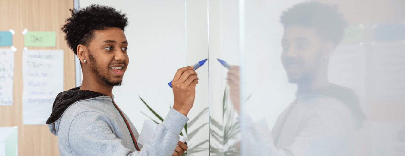 Schüler schreibt im Alphabetisierungsunterricht lächelnd an die Tafel