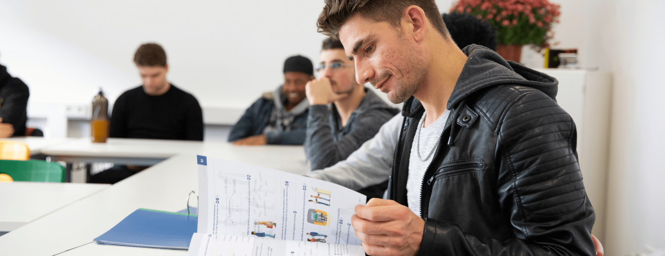 Schüler sitzt im Klassenraum und blättert durch DaZ-Lernmaterial
