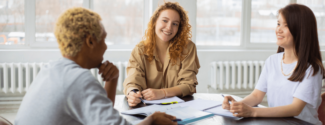 Drei junge Frauen sitzen an einem Tisch und haben Unterrichtsmaterialien für DaZ vor sich liegen