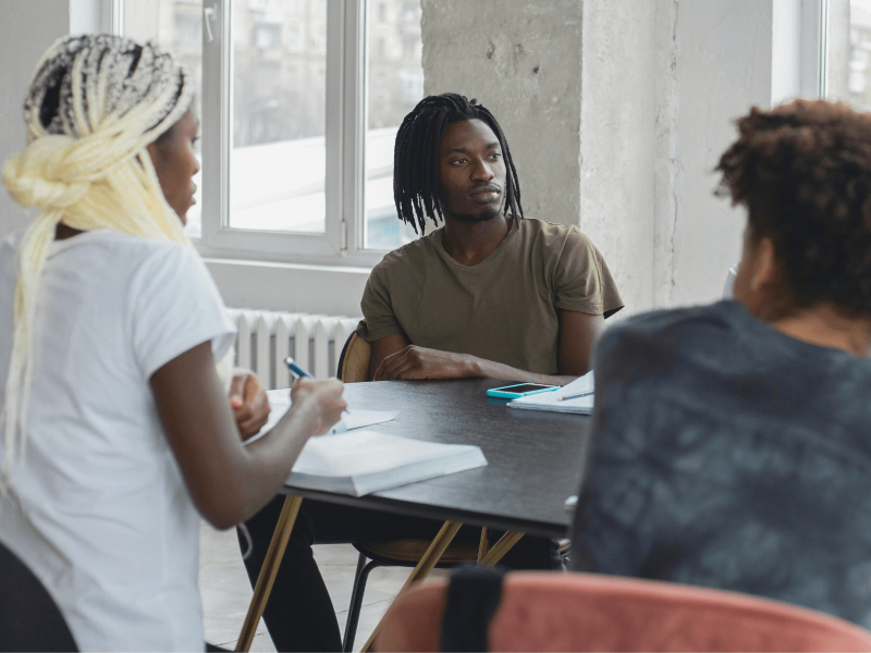 drei DaZ-Schüler*innen sitzen am Tisch im Klassenzimmer und lernen sich kennen